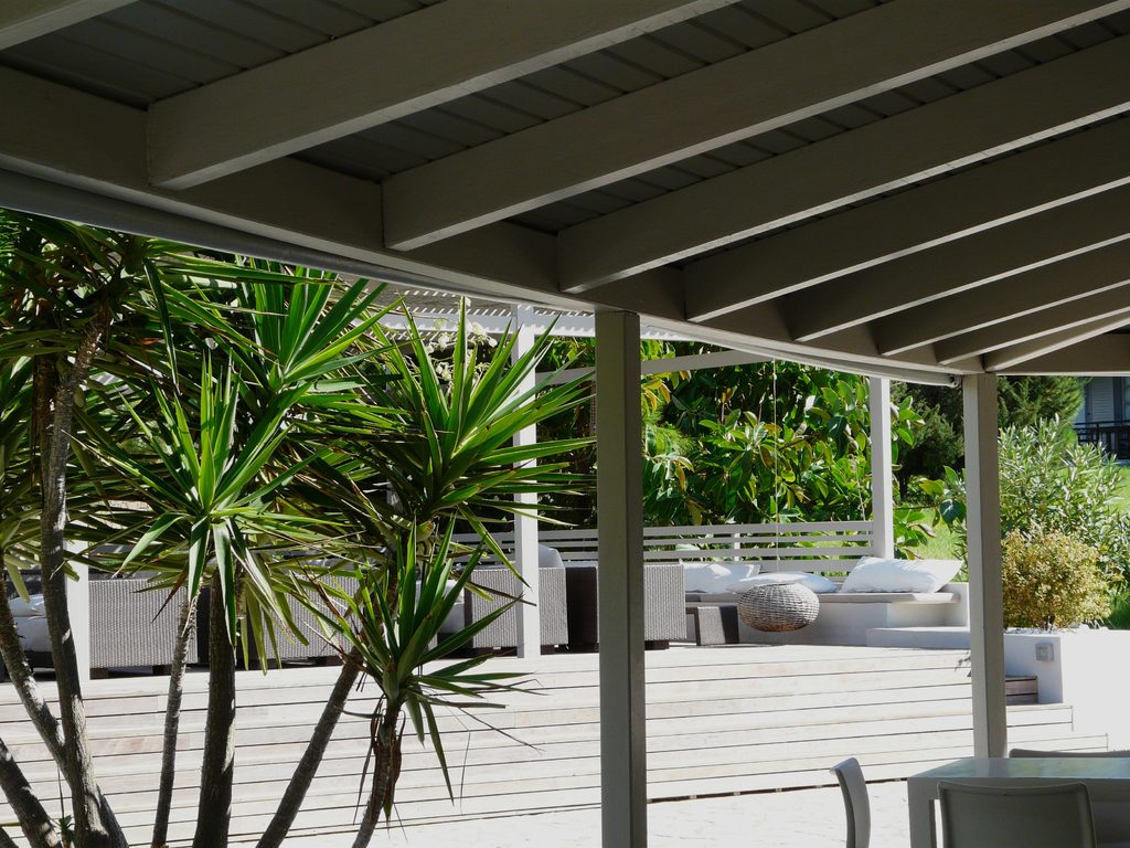Covered deck with white outdoor seating framed by palms and tropical plants