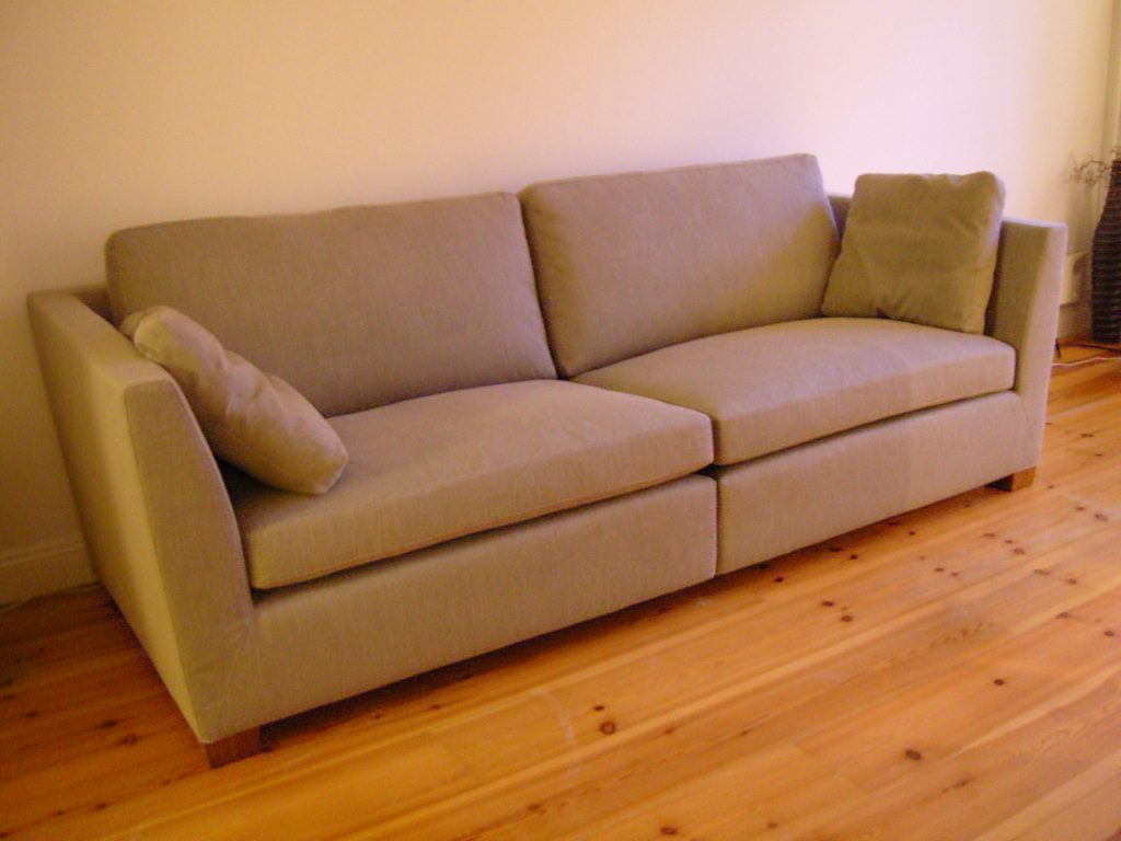 Bright living room with a tan fabric sofa against a white wall on a warm pine floor