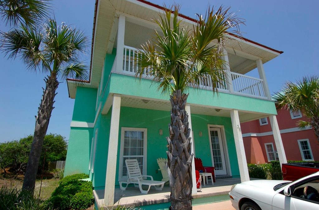 Mint green two storey home with white porches and tall palm trees