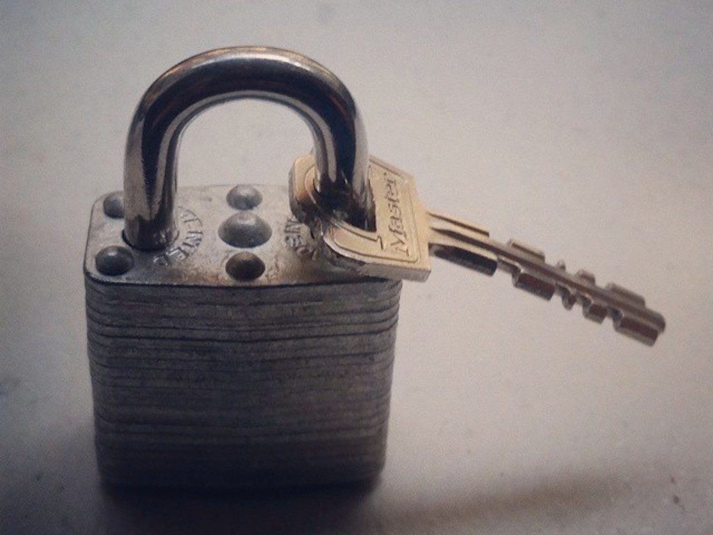 Heavy steel padlock with a key in the lock on a pale background